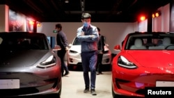 FILE PHOTO: A man wearing a face mask following the coronavirus disease (COVID-19) outbreak walks by Tesla Model 3 sedans and Tesla Model X sport utility vehicle at a new Tesla showroom in Shanghai, China May 8, 2020. REUTERS/Yilei Sun/File Photo