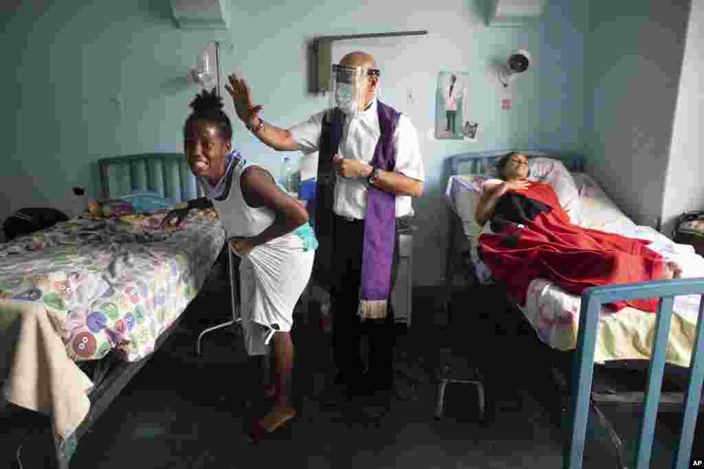 Katolički sveštenik, centar, moli se nad ženom koja plače, rekavši da je fizički boli, dok je smeštena u bolnici u Karakasu, u Venecueli u jeku epidemije koronevirusa. 11. maj. 2021. ( Foto: Arijana Kubiljos / AP )
