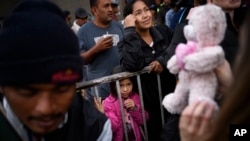 Una niña de Honduras espera el regalo de una organización no gubernamental fuera de un refugio para los migrantes donde muchos esperan para solicitar asilo a EE.UU., en el centro de Tijuana, México, el martes 25 de diciembre de 2018.