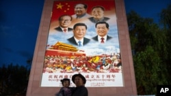 FILE - A man holds a girl in front of a large mural depicting Chinese President Xi Jinping and other Chinese leaders at a public square at the base of the Potala Palace in Lhasa in western China's Tibet Autonomous Region, June 1, 2021. (AP Photo/Mark Schiefelbein)