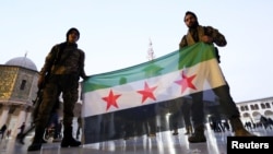 Rebel fighters pose as they hold a Syrian opposition flag inside the Umayyad Mosque, after rebels seized the capital and ousted Syria's Bashar al-Assad, in Damascus, Syria December 9, 2024.