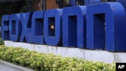 FILE - A worker looks out through the logo at the entrance of the Foxconn complex in the southern Chinese city of Shenzhen, May 27, 2010. 