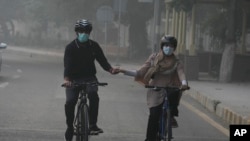 Warga tampak mengenakan masker saat bersepeda di jalanan Kota Lahore, Pakistan, pada 3 November 2024. (Foto: AP/K. M. Chaudary)