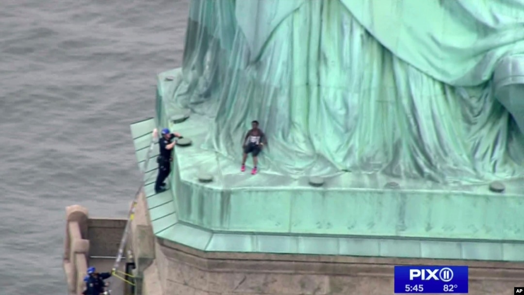 In this image made from video by WPIX-TV, a woman leans against the robes of the Statue of Liberty on Liberty Island, as a police officer stands on a ledge nearby, talking the climber into descending, in New York, July 4, 2018.