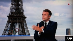 This photograph shows a television screen broadcasting France's President Emmanuel Macron on French TV channel France 2, on a set installed on the roof of the Musee de l'Homme (Museum of Mankind) at the Trocadero, with the Eiffel Tower seen in the background, on July 23, 2024.