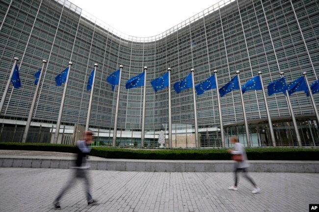 FILE - European Union flags wave in the wind as pedestrians walk by EU headquarters in Brussels, on Sept. 20, 2023. (AP Photo/Virginia Mayo, File)