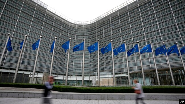 FILE - European Union flags wave in the wind as pedestrians walk by EU headquarters in Brussels, on Sept. 20, 2023. (AP Photo/Virginia Mayo, File)