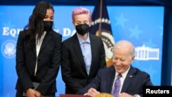 U.S. Women's National Soccer Team players Margaret Purce and Megan Rapinoe peek over U.S. President Joe Biden’s shoulder as he signs an Equal Pay Day proclamation at the White House in Washington, March 24, 2021. 
