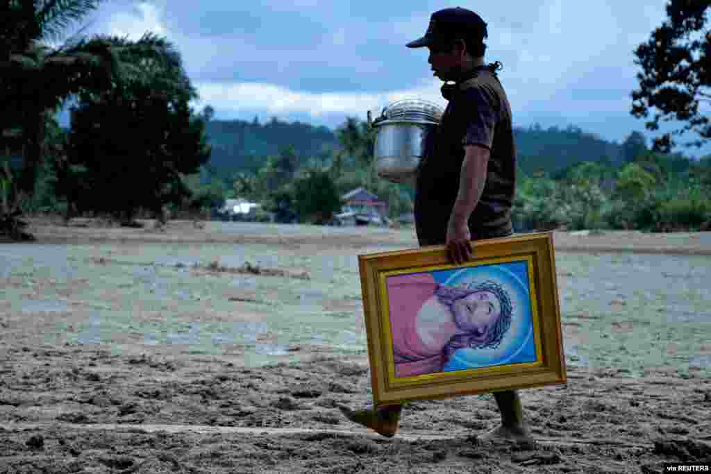 A man walks through mud with a frame depicting Jesus Christ, following flash floods that left several dead and dozens missing, in North Luwu, South Sulawesi, Indonesia, July 18, 2020, in this Antara Foto.