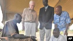 FILE - Former U.S. President and Carter Center Founder Jimmy Carter watches while Garbino, a young farmer with a Guinea worm disease, receives free treatment from a village volunteer trained by The Carter Center in partnership with the Government of Southern Sudan’s Guinea Worm Eradication Program,Terekeka, Southern Sudan, Feb. 11, 2010.