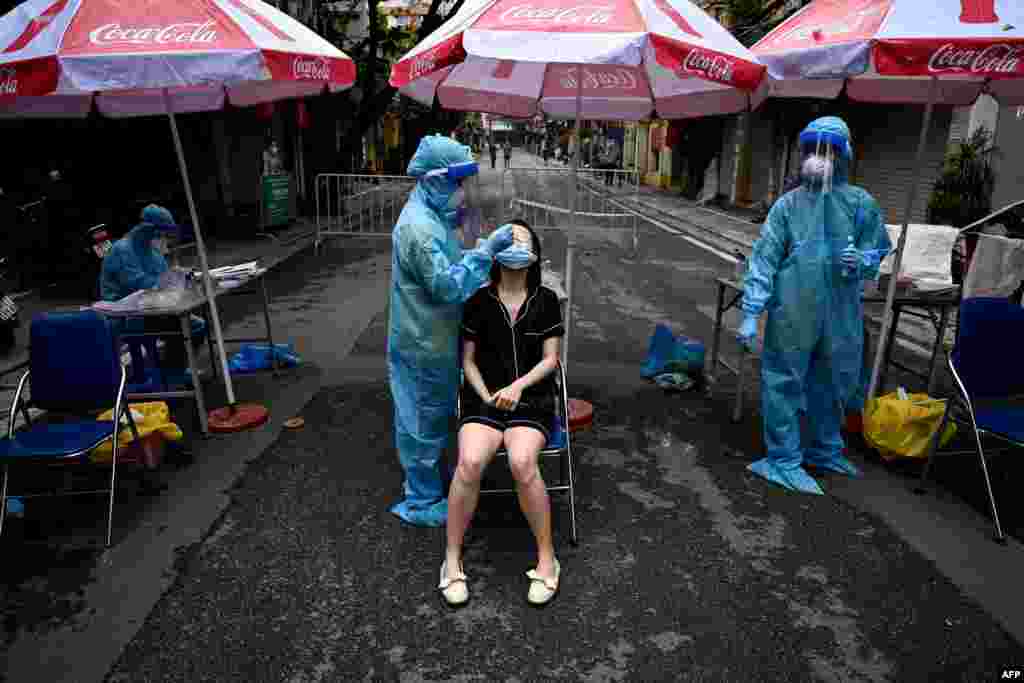A health worker wearing personal protective equipment (PPE) collects swab samples from a woman (C) for Covid-19 testing in the Old Quarter in Hanoi, Vietnam.