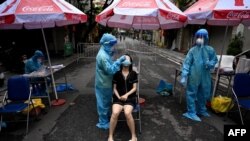 A health worker wearing personal protective equipment (PPE) collects swab samples from a woman (C) for Covid-19 testing in the Old Quarter in Hanoi, Vietnam.