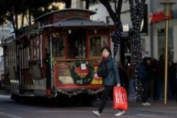 A woman carries a shopping bag while walking in front of a cable car in San Francisco, Nov. 29, 2019.