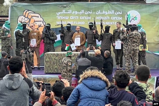 Palestinian Hamas fighters escort Israeli hostages Ohad Ben Ami, Eli Sharabi and Or Levy on a stage before handing them over to a Red Cross team in Deir el-Balah, central Gaza, Feb. 8, 2025.