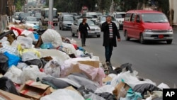 In this Thursday, Dec. 17, 2015 photo, Lebanese citizens pass by a pile of garbage on a street in Beirut, Lebanon. 