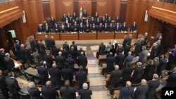 Photo released by the Lebanese Parliament media office, shows new cabinet members, background, and Lebanese lawmakers, foreground standing before a debate for a vote of confidence, in the Lebanese parliament, in Beirut, Feb. 12, 2019. 