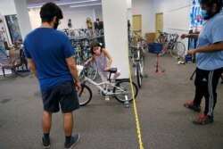 Mahdi Hashemian, of Cambridge, Mass., left, watches as his daughter Zeynab climbs onto her first bicycle as technician Dell Wilkerson Jr. looks on at Spokehouse Bikes in the Upham's Corner neighborhood of Boston, June 24, 2020.