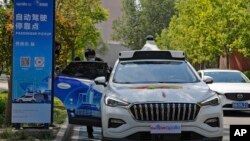 Seorang pria mengenakan masker masuk ke Baidu Apollo Robotaxi di tempat penjemputan penumpang di Taman Shougang, Beijing, Minggu, 2 Mei 2021. (AP Photo/Andy Wong)