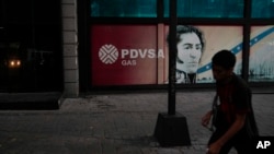 ARCHIVO: Un peatón camina junto a un cartel de Petróleos de Venezuela, S.A, PDVSA, y una imagen del héroe de la independencia venezolana Simón Bolívar, en Caracas, Venezuela, el 20 de marzo de 2023. 