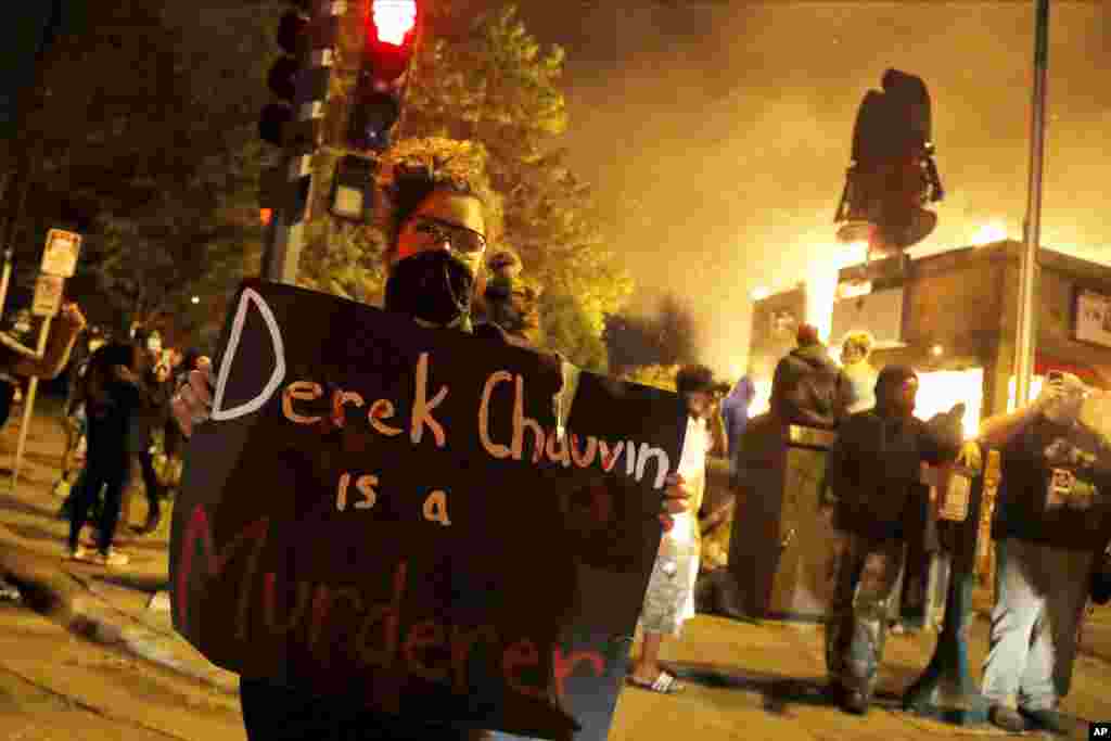 A protester holds a sign in front of a fire at a restaurant, early Friday, May 29, 2020, in Minneapolis. Protests over the death of George Floyd, a black man who died in police custody Monday, broke out in Minneapolis for a third straight night. (AP Photo/Julio Cortez)