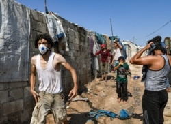 FILE - A man wearing a gas mask walks past a make-shift brick shelter for displaced Syrians during clashes between Syrian demonstrators and members of the Turkish gendarmerie near the town of Atme in the northwestern Idlib province, Aug. 30, 2019.