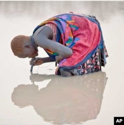 FILE - A young herder in Kuse Dam, Southern Sudan, uses a pipe filter provided by The Carter Center to strain out infective Guinea worm larvae from the water while drinking, Feb. 6, 2010.