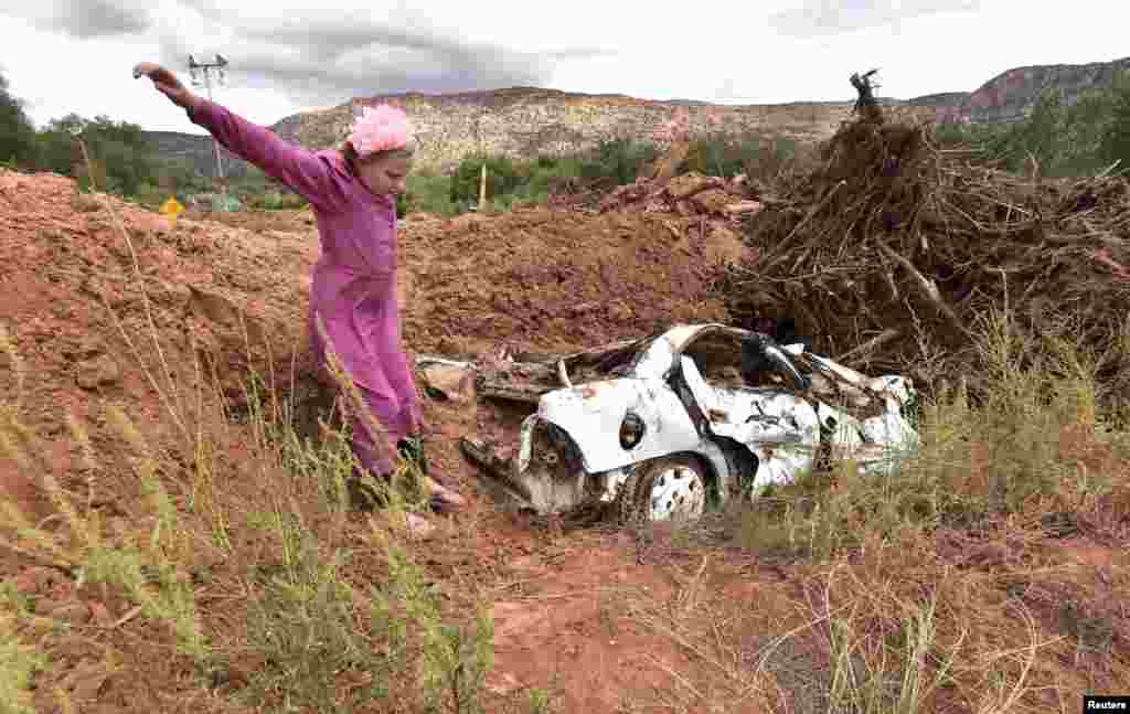 A girl jumps off a mound of dirt that was piled up with one of the vehicles found after a flash flood, in Hildale, Utah, Sept. 15, 2015. Flash floods killed nine people near Utah's border with Arizona when a "large wall of water" triggered by heavy rain pounding nearby canyons swept them away in their cars, officials said.
