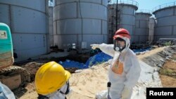 Japan's Economy, Trade and Industry Minister Toshimitsu Motegi (R), wearing a protective suit and a mask, inspects contaminated water tanks at the tsunami-crippled Fukushima Daiichi nuclear power plant in Fukushima prefecture August 26, 2013, in this phot