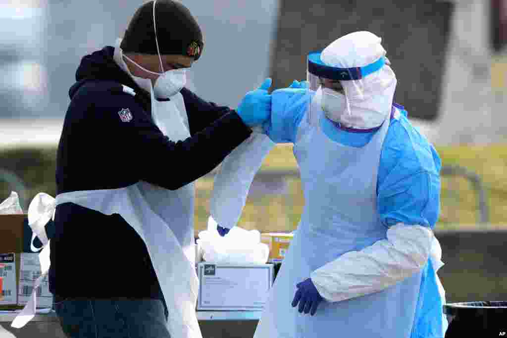 Medical personnel help each other at a federal coronavirus drive-thru testing site in the parking lot of Walmart in North Lake, Illinois, March 25, 2020.