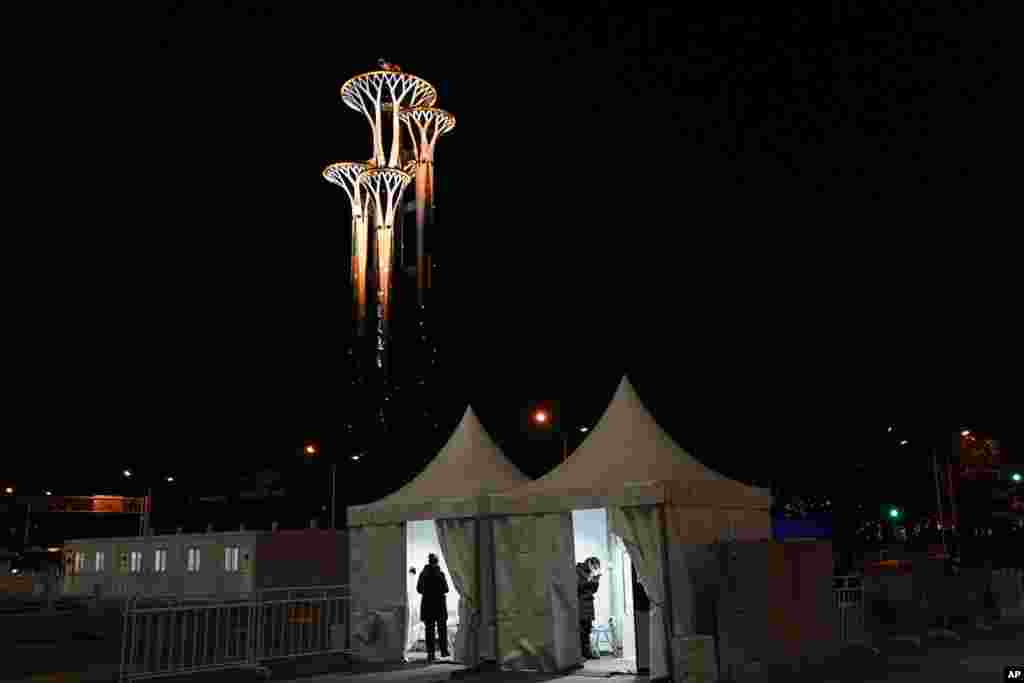 Two Olympic workers stand in their shelter with the Beijing Olympic Tower in the background, on the day before the Lunar New Year, ahead of the 2022 Winter Olympics in Beijing, China.