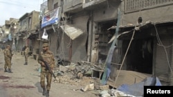 A security official walks in front of a damaged shop after a remote control bomb blast took place near a Shi'ite procession in Dera Ismail Khan in Pakistan's northwest, November 25, 2012. 