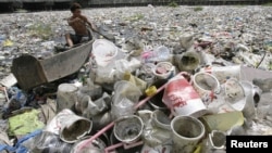 Một bé trai nhặt các đồ nhựa trôi trên con sông phủ đầy rác ở Manila