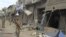 A security official walks in front of a damaged shop after a remote control bomb blast took place near a Shi'ite procession in Dera Ismail Khan in Pakistan's northwest, November 25, 2012. 