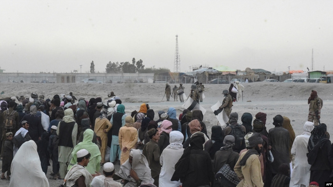 FILE - Stranded people wait at the Spin Boldak border crossing point guarded by security personnel in Pakistan's border town of Chaman, July 16, 2021. Taliban insurgents closed the crossing point August 6, 2021. 