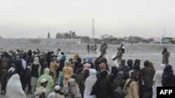 FILE - Stranded people wait at the Spin Boldak border crossing point guarded by security personnel in Pakistan's border town of Chaman, July 16, 2021. Taliban insurgents closed the crossing point August 6, 2021. 