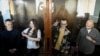 From left, Russian journalists Konstantin Gabov, Antonina Favorskaya, Artyom Kriger and Sergey Karelin stand behind a glass wall of an enclosure for defendants as they attend a court hearing in Moscow on Oct. 2, 2024.