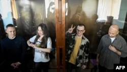 From left, Russian journalists Konstantin Gabov, Antonina Favorskaya, Artyom Kriger and Sergey Karelin stand behind a glass wall of an enclosure for defendants as they attend a court hearing in Moscow on Oct. 2, 2024.