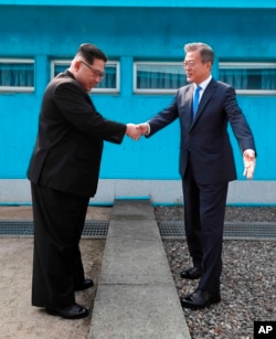 North Korean leader Kim Jong Un, left, shakes hands with South Korean President Moon Jae-in over the military demarcation line at the border village of Panmunjom in Demilitarized Zone, April 27, 2018.