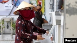 A woman fills a plastic bag with rice from a 24/7 automatic rice dispensing machine 'Rice ATM' during the outbreak of the coronavirus disease (COVID-19), in Ho Chi Minh, Vietnam, April 11, 2020. (REUTERS/Yen Duong)