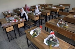 FILE-in this May 16, 2021 file photo, Schoolgirls sit inside a classroom with bouquets of flowers on empty desks as a tribute to those killed in the brutal May 8 bombing of the Syed Al-Shahda girls school, in Kabul, Afghanistan.