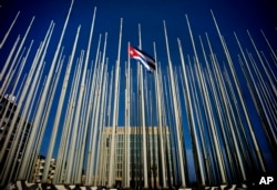 A Cuban flag flies among empty flag polls near the U.S. Interests Section building, behind, in Havana, Sunday, July 19, 2015.