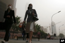 Office workers wearing face masks walk on a street as Beijing is hit by polluted air and sandstorm, May 4, 2017.