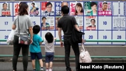 Une famille regarde les affiches des candidats devant un bureau de vote à Tokyo, au Japon, le 5 juillet 2020