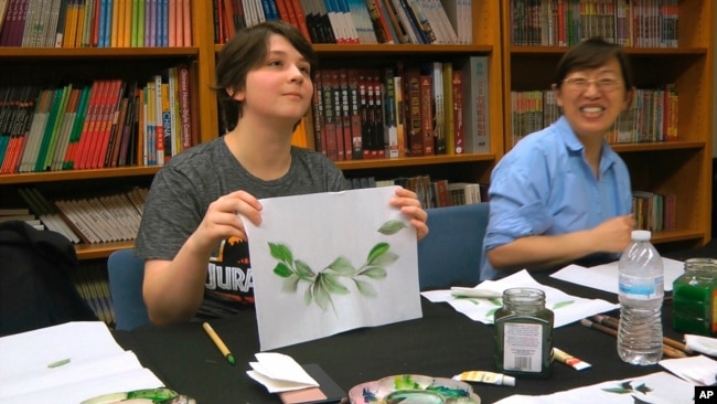 FILE - A student, left, shows her painting at a traditional Chinese painting class at the Confucius Institute at George Mason University in Fairfax, Virginia on May 2, 2018.