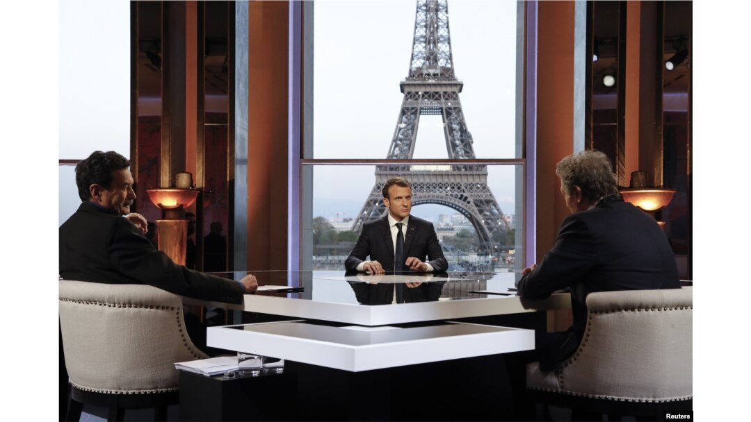 French President Emmanuel Macron (C) poses on the TV set before an interview with BFM journalist Jean-Jacques Bourdin (R) and Mediapart investigative website journalist Edwy Plenel (L), at the Theatre National de Chaillot across from the Eiffel Tower in Paris, April 15, 2018.