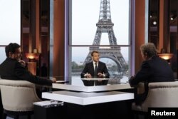 French President Emmanuel Macron (C) poses on the TV set before an interview with BFM journalist Jean-Jacques Bourdin (R) and Mediapart investigative website journalist Edwy Plenel (L), at the Theatre National de Chaillot across from the Eiffel Tower in Paris, April 15, 2018.