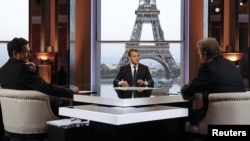 Presiden Perancis Emmanuel Macron (tengah) berpose di depan TV sebelum wawancara dengan wartawan BFM, Jean-Jacques Bourdin (kanan) dan wartawan situs web berita investigasi Mediapart, Edwy Plenel (kiri), di Theatre National de Chaillot di seberang Menara Eiffel di Paris, 15 April 2018. 