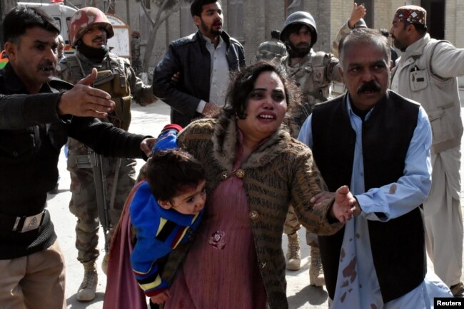 FILE - A policeman guides a family away from the Bethel Memorial Methodist Church in Quetta, Pakistan, after gunmen attacked, Dec. 17, 2017.