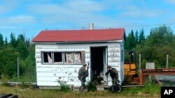 In this recent photo RCMP officers canvas homes and buildings in the Gillam, Manitoba area, as they continue to search for two teenagers being sought in the killings of three people in northern British Columbia.