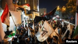 دیمەنی کۆبوونەوەی چەند خۆپیشاندەرێکی لایەنگری حەشدی شەعبی لەبەردەم باڵیۆزخانەی ئێران لە بەغدا دوای ڕاگەیاندنی ئاگربەستی نێوان ئەمەریکا و ئێران لە ڕۆژی 8ی چوای 2026.